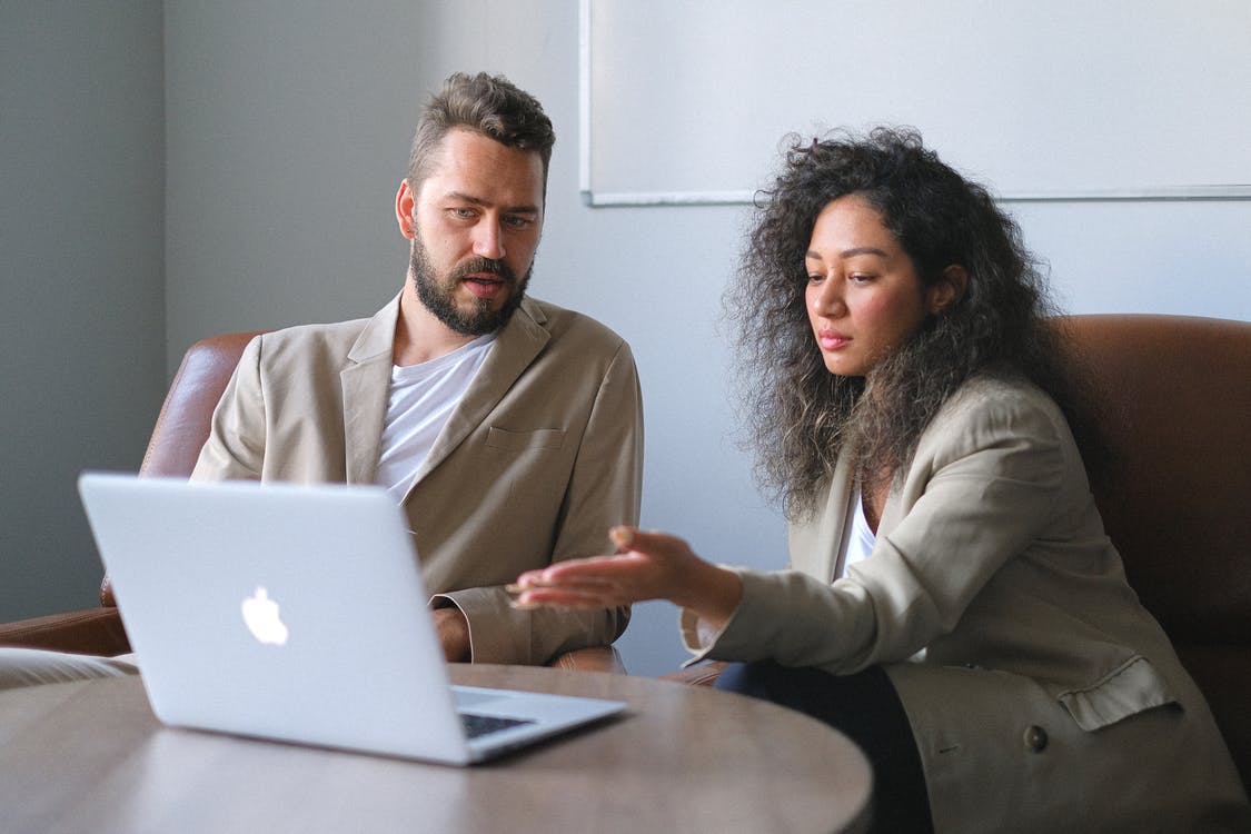 Free Serious colleagues in stylish outfits sitting at table and using laptop while discussing new project in office Stock Photo
